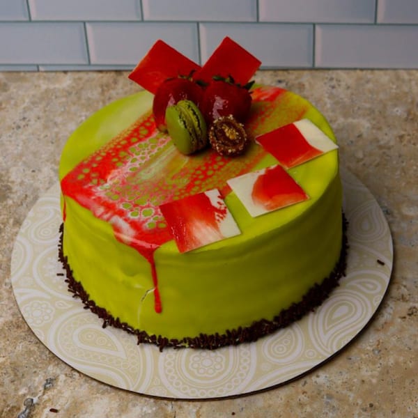 Vibrant green cake with red and white frosting, topped with strawberries, a green macaron, and chocolate.