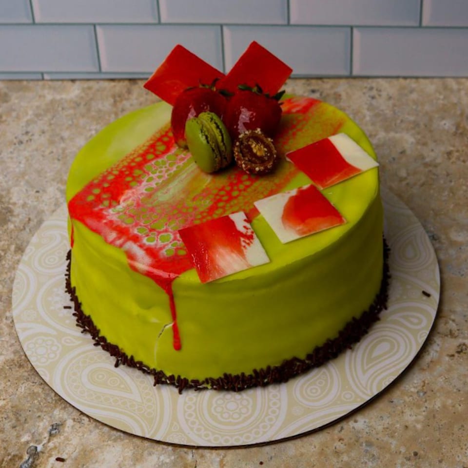 Vibrant green cake with red and white frosting, topped with strawberries, a green macaron, and chocolate.