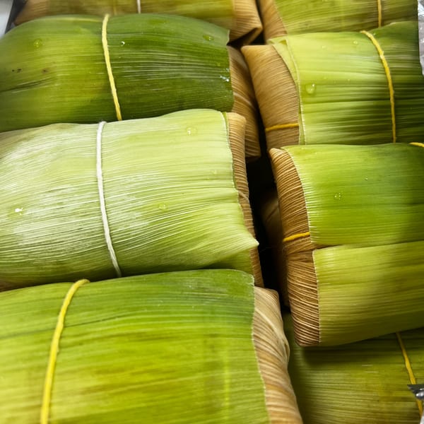 Several Brazilian pamonhas, wrapped in green and tan corn husks, tied with string.