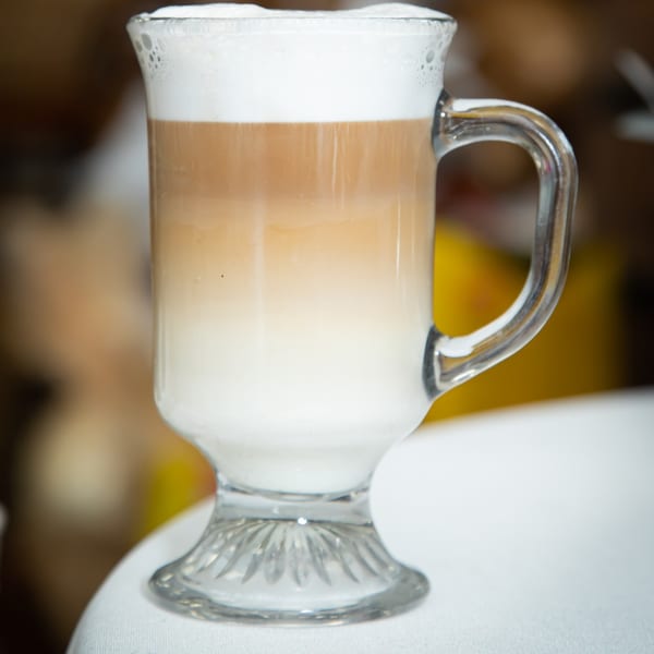 A tall glass mug of layered latte with frothy white foam on top.