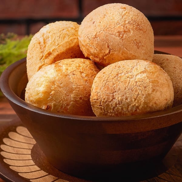 A dark bowl filled with golden-brown Brazilian Pão de Queijo, or cheese bread, on a wooden tray.