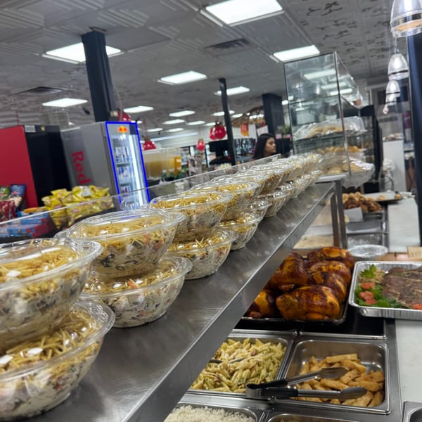 Rows of Brazilian food in clear containers, including chicken, pasta, and rice, at Minas Grill & Market.