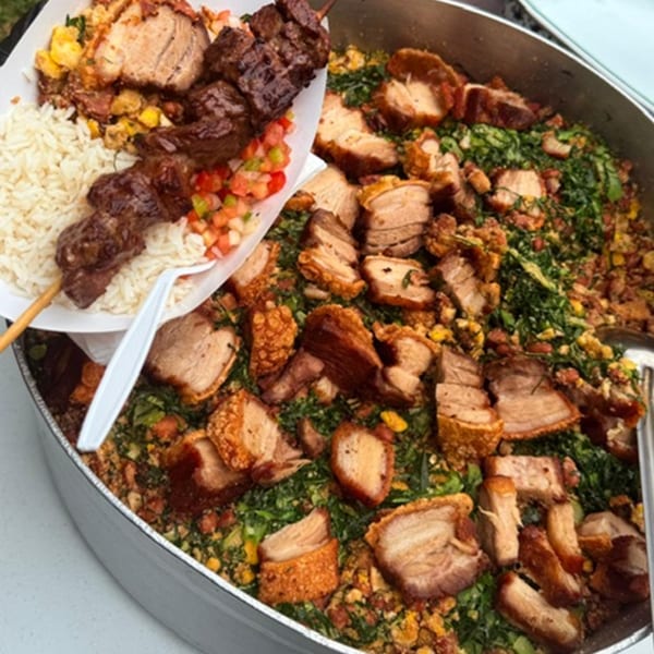 A Brazilian meal with a beef skewer, rice, and salsa, alongside a large pan of pork belly and greens.