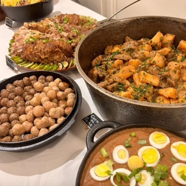 A buffet spread of Brazilian dishes, including meat, potatoes, fried dough balls, and a stew with eggs.