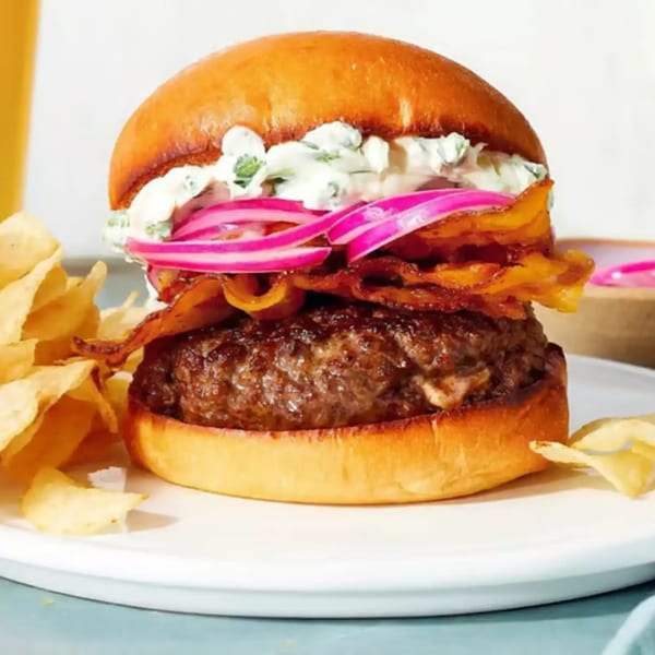 Minas Grill & Market's burger with bacon, pickled red onions, and creamy sauce, served with chips.