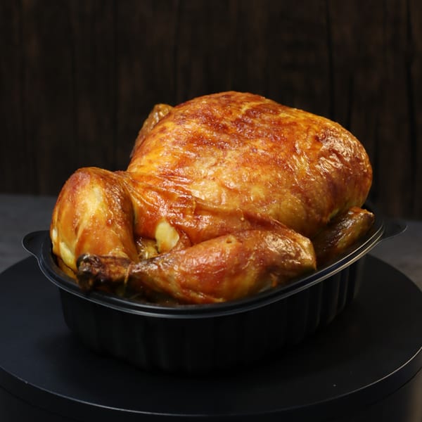 Whole roasted chicken with crispy golden-brown skin in a black takeout container.