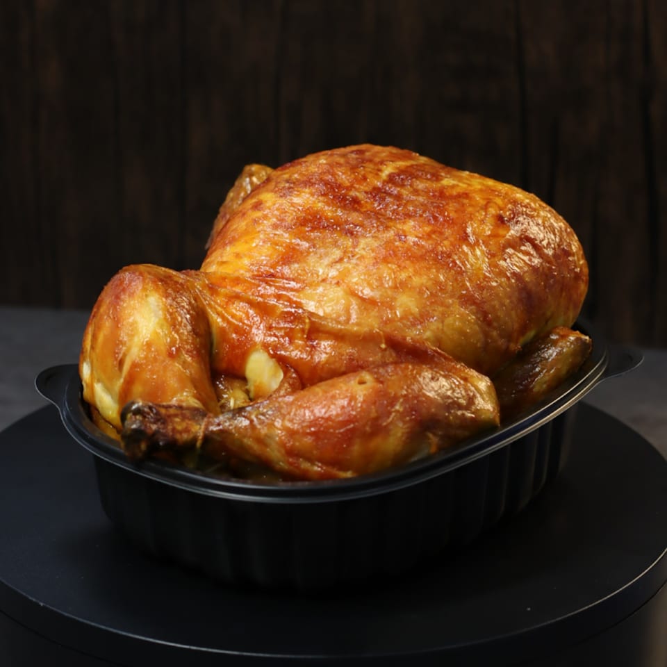 Whole roasted chicken with crispy golden-brown skin in a black takeout container.