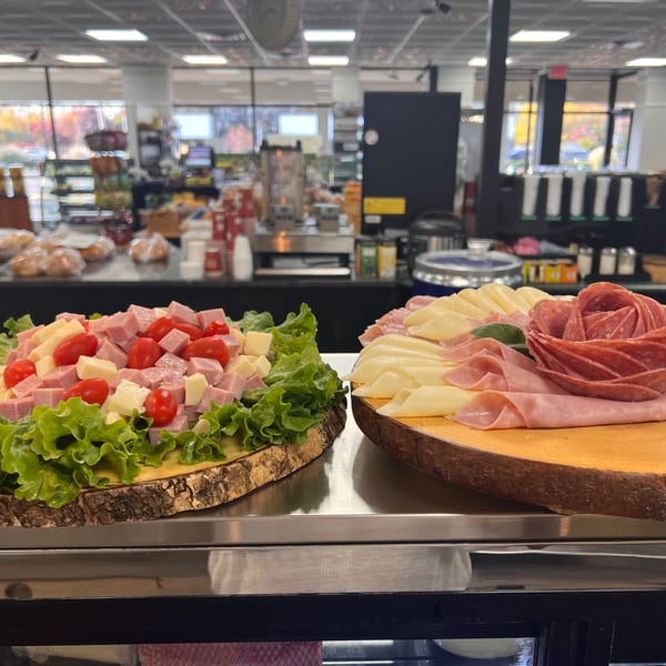 Two wooden platters with charcuterie, one with cubed ham, cheese, and tomatoes, the other with sliced meats and cheese.